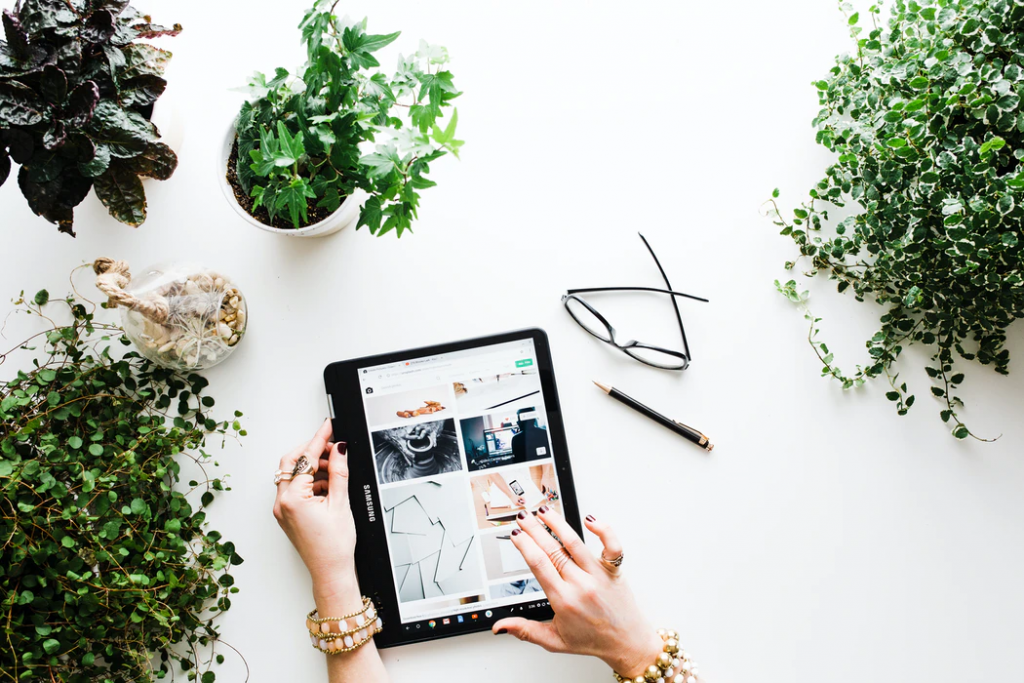 A womanâs hands working with a tablet on a table covered in potted plants.
